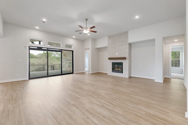 unfurnished living room with a tile fireplace, ceiling fan, and light wood-type flooring