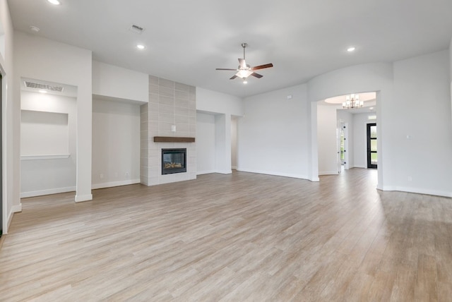 unfurnished living room with ceiling fan with notable chandelier, a tile fireplace, and light hardwood / wood-style flooring