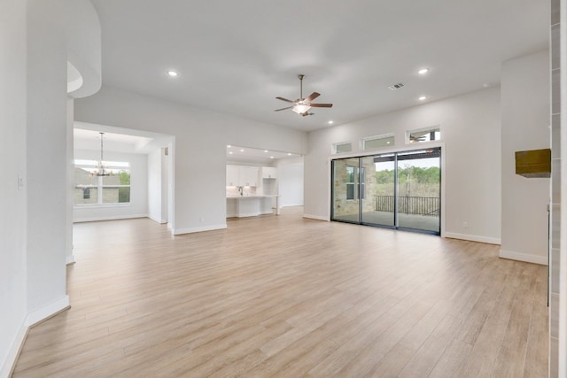 unfurnished living room featuring ceiling fan with notable chandelier and light wood-type flooring