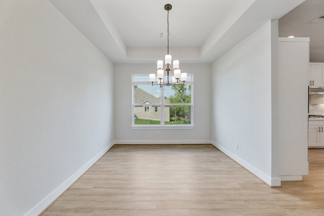 spare room with light hardwood / wood-style flooring, a notable chandelier, and a tray ceiling