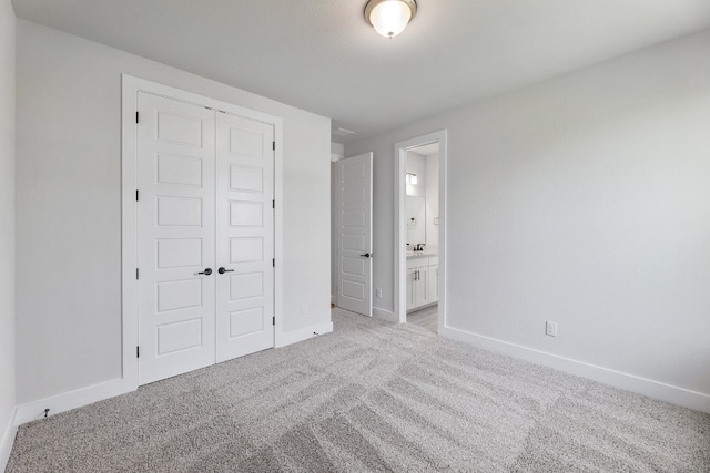 unfurnished bedroom with light carpet, ensuite bath, a closet, and sink