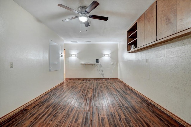 empty room with ceiling fan, dark wood-type flooring, and built in shelves