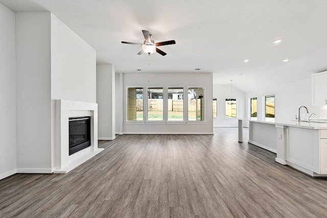 unfurnished living room featuring hardwood / wood-style flooring, sink, lofted ceiling, and ceiling fan