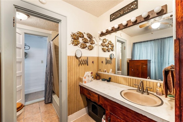 bathroom with a textured ceiling, tile floors, ceiling fan, and vanity with extensive cabinet space