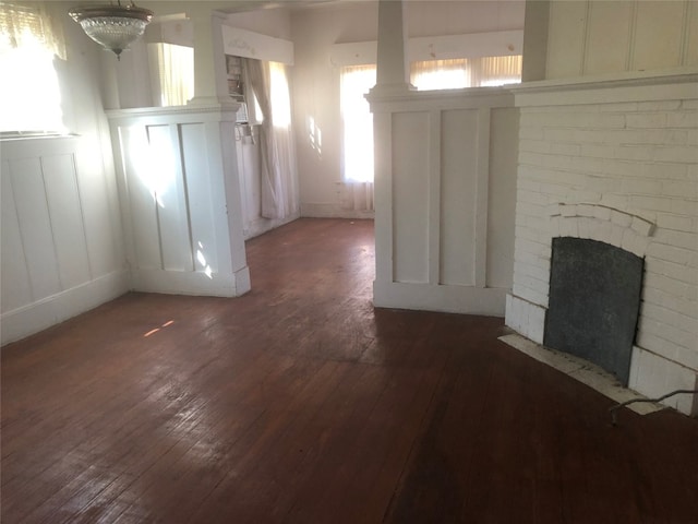 unfurnished living room with brick wall, a brick fireplace, and dark wood-type flooring