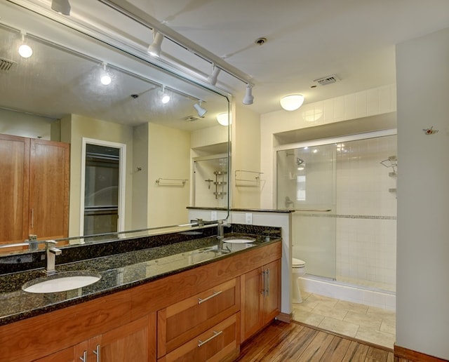 bathroom featuring double vanity, a shower with shower door, toilet, and tile floors