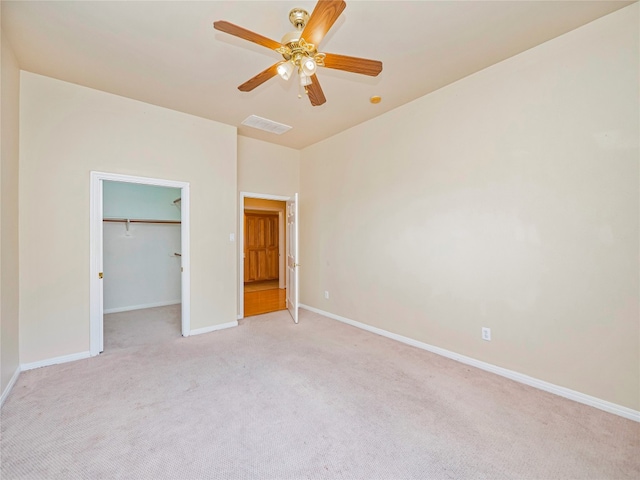 unfurnished bedroom with light carpet, a spacious closet, and ceiling fan