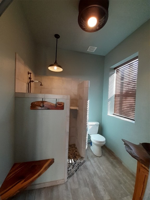 bathroom featuring toilet, a tile shower, and wood-type flooring