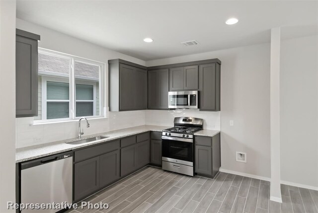 kitchen with light wood-type flooring, light stone countertops, sink, appliances with stainless steel finishes, and gray cabinets