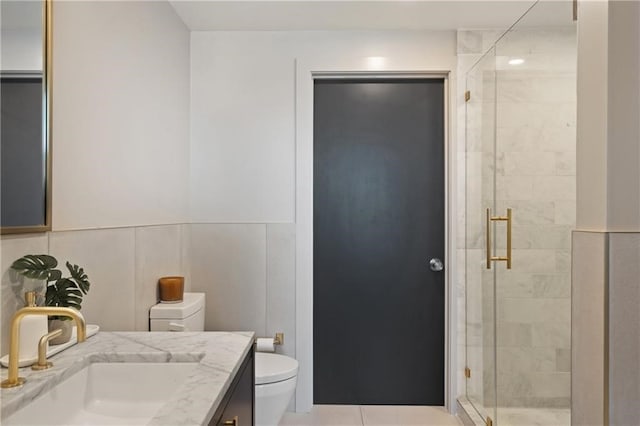 bathroom featuring tile walls, toilet, vanity with extensive cabinet space, a shower with door, and tile floors