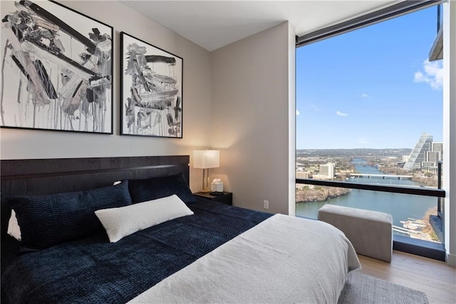 bedroom with expansive windows, a water view, and light hardwood / wood-style flooring