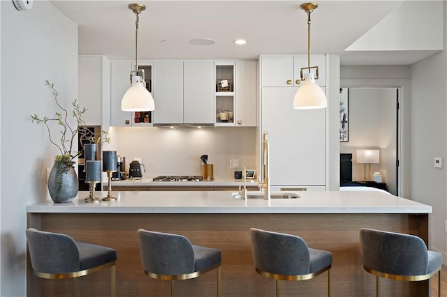 kitchen featuring hanging light fixtures, a kitchen breakfast bar, white cabinetry, and sink