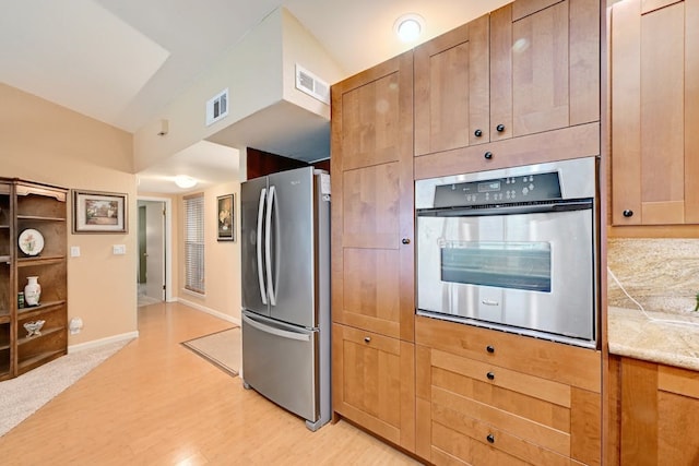 kitchen with appliances with stainless steel finishes, light hardwood / wood-style flooring, and light stone counters