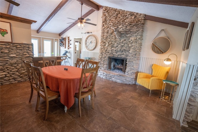 tiled dining area with ceiling fan, a stone fireplace, vaulted ceiling with beams, and a textured ceiling