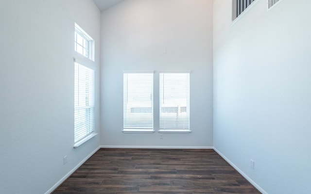 empty room with a high ceiling, plenty of natural light, and dark hardwood / wood-style flooring