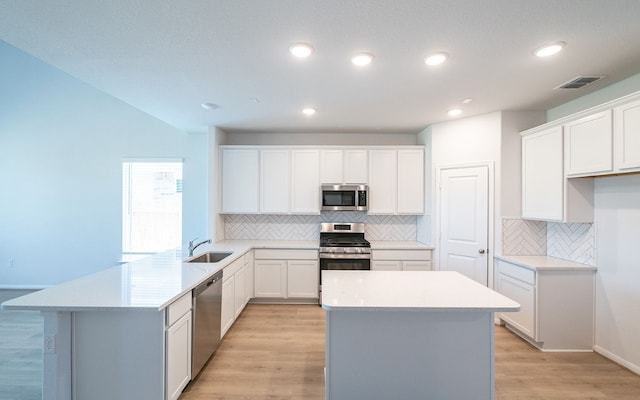 kitchen with stainless steel appliances, a center island, light hardwood / wood-style flooring, white cabinets, and backsplash