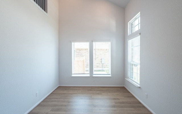 unfurnished room featuring light hardwood / wood-style flooring, a towering ceiling, and a wealth of natural light