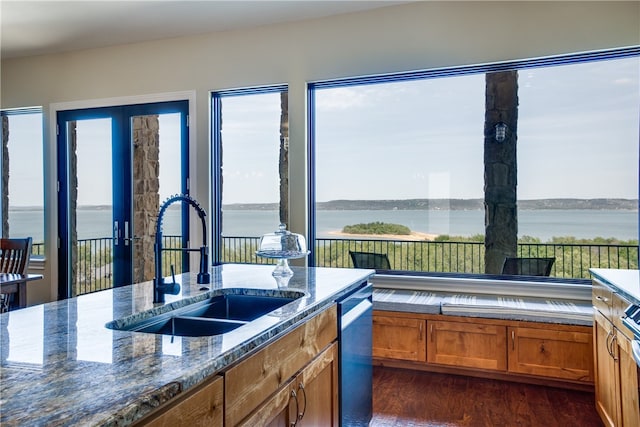 kitchen with dark wood-type flooring, sink, a water view, dark stone countertops, and dishwasher