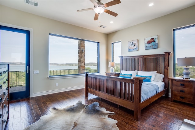 bedroom with dark hardwood / wood-style flooring, ceiling fan, a water view, and access to exterior