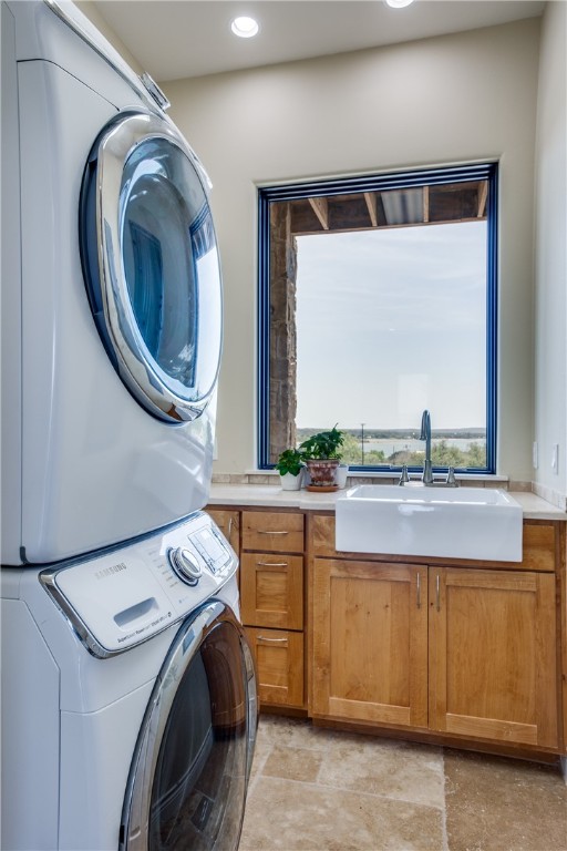 laundry area with stacked washer / dryer, cabinets, sink, and light tile floors