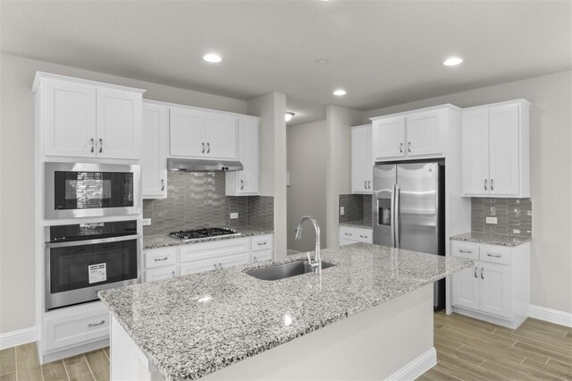 kitchen with appliances with stainless steel finishes, white cabinets, light wood-type flooring, a kitchen island with sink, and sink