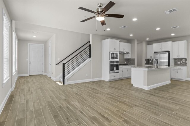 kitchen featuring ceiling fan, a center island with sink, stainless steel appliances, and light wood-type flooring