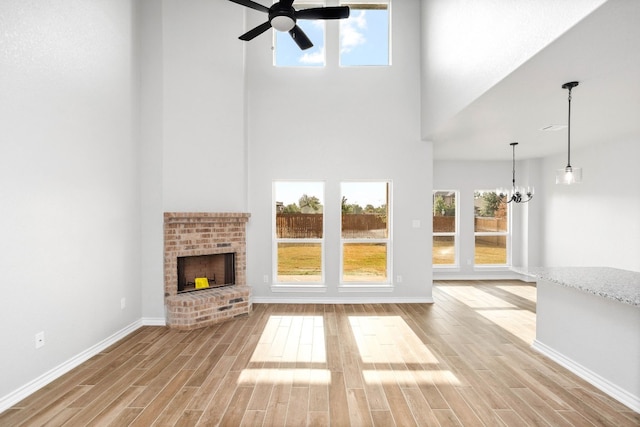 unfurnished living room with a healthy amount of sunlight, a brick fireplace, a towering ceiling, and ceiling fan with notable chandelier