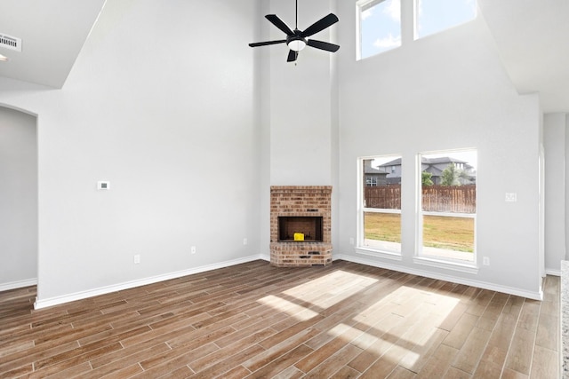 unfurnished living room with light hardwood / wood-style floors, a fireplace, ceiling fan, and a high ceiling