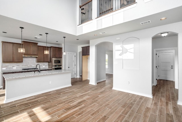 kitchen featuring an island with sink, light stone counters, backsplash, stainless steel appliances, and light wood-type flooring