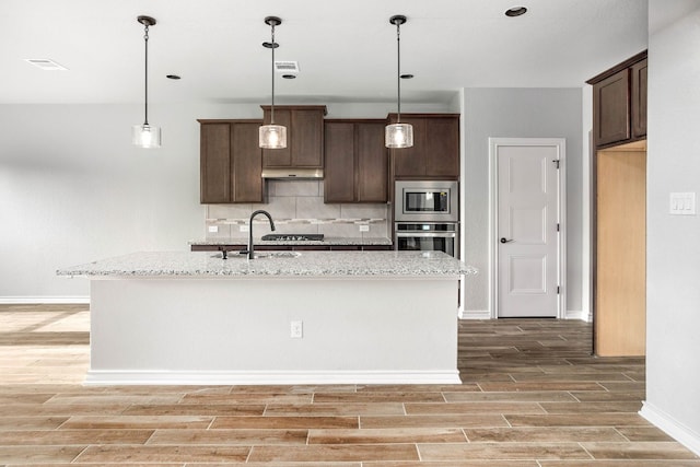 kitchen featuring light stone countertops, appliances with stainless steel finishes, tasteful backsplash, dark brown cabinetry, and pendant lighting