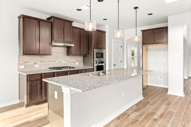 kitchen featuring backsplash, hanging light fixtures, an island with sink, and stainless steel appliances