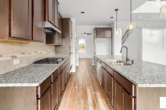 kitchen with appliances with stainless steel finishes, light stone counters, an island with sink, pendant lighting, and sink