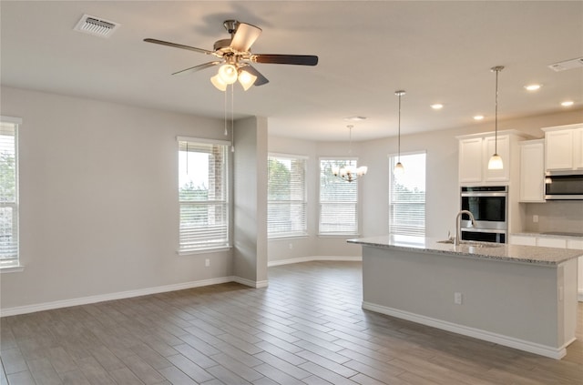 kitchen with appliances with stainless steel finishes, light wood-type flooring, light stone counters, ceiling fan with notable chandelier, and white cabinetry