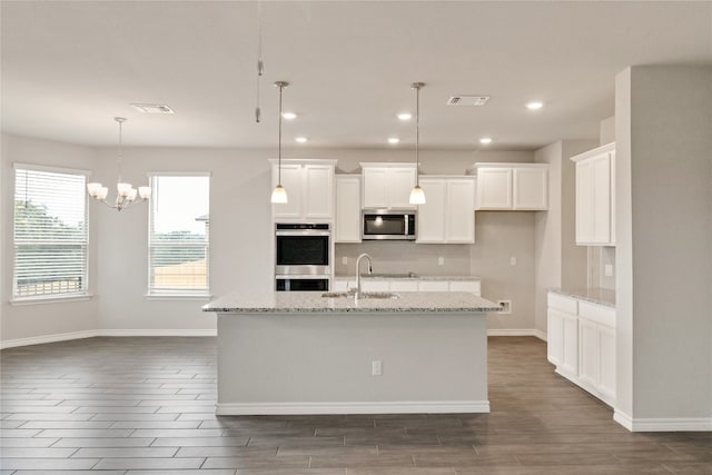 kitchen with appliances with stainless steel finishes, decorative light fixtures, white cabinetry, and a kitchen island with sink