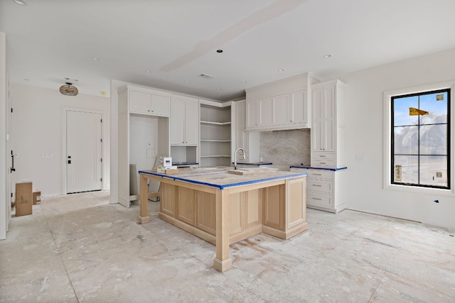 kitchen featuring white cabinets, an island with sink, a sink, open shelves, and backsplash