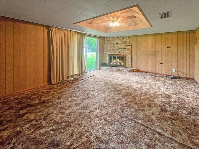 unfurnished living room featuring wood walls, a fireplace, ceiling fan, and carpet