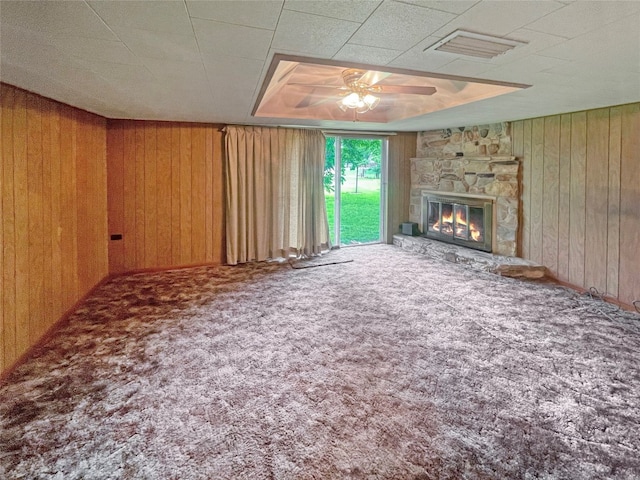 unfurnished living room with carpet floors, wooden walls, ceiling fan, and a fireplace