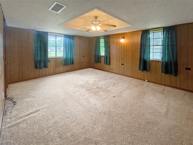 carpeted spare room featuring wooden walls and ceiling fan