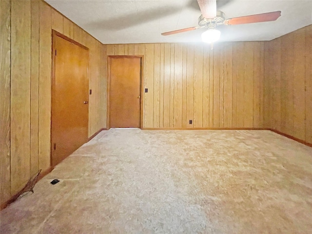 carpeted empty room featuring wood walls and ceiling fan