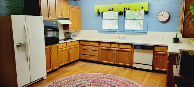 kitchen featuring under cabinet range hood, white appliances, a sink, light wood-style floors, and brown cabinets