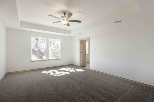 empty room featuring ceiling fan, light colored carpet, and a raised ceiling