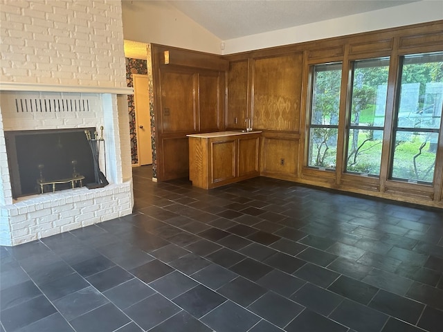 unfurnished living room with a fireplace, dark tile flooring, lofted ceiling, and brick wall