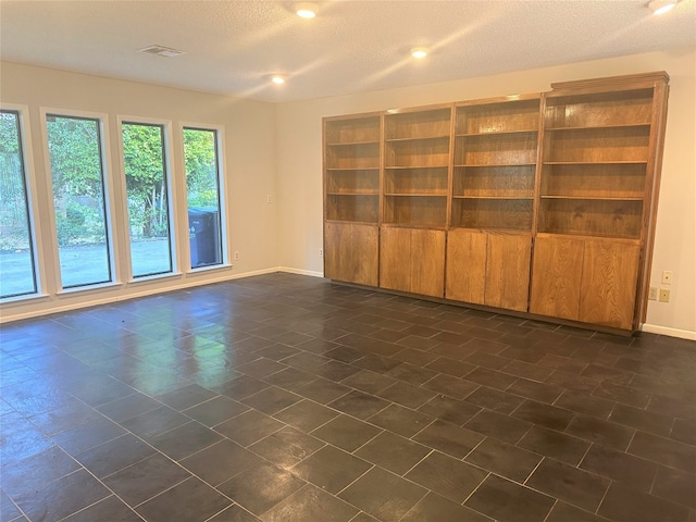 empty room featuring a textured ceiling and dark tile flooring