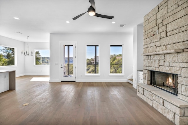 unfurnished living room with a stone fireplace, hardwood / wood-style flooring, and ceiling fan with notable chandelier