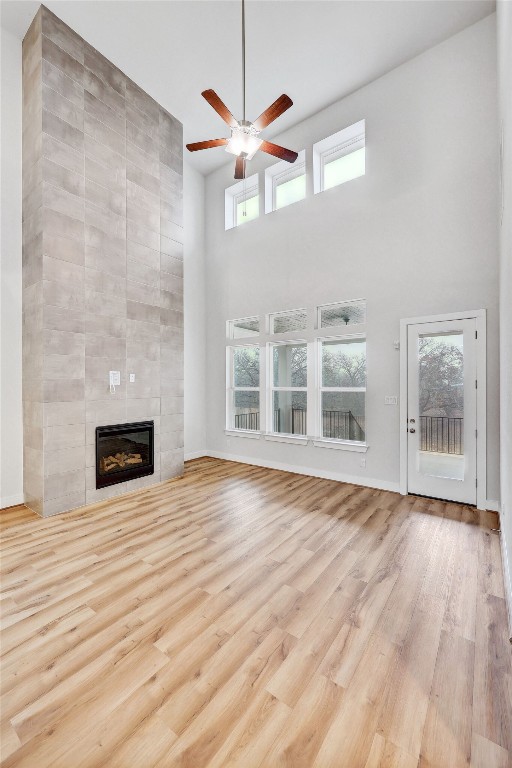 unfurnished living room with ceiling fan, a tiled fireplace, a wealth of natural light, and a high ceiling