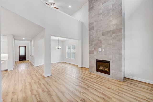 unfurnished living room featuring a tile fireplace, light hardwood / wood-style flooring, ceiling fan with notable chandelier, and a towering ceiling