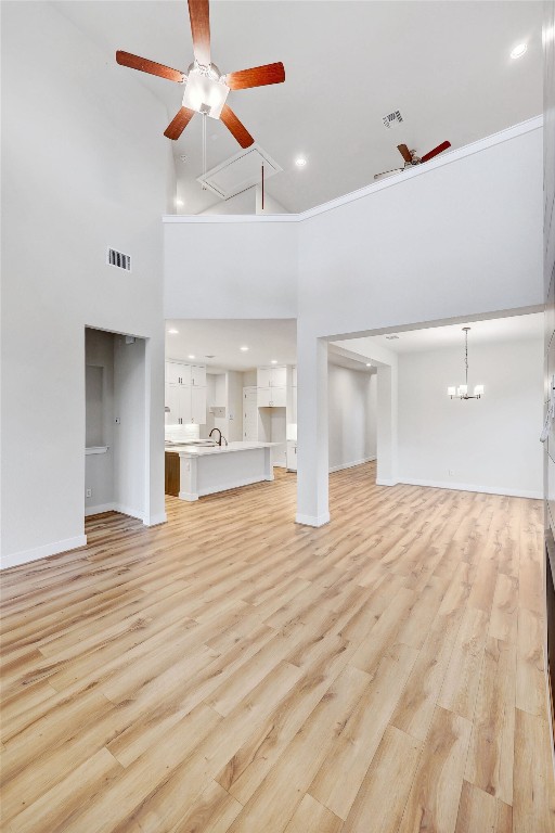 unfurnished living room with light hardwood / wood-style floors, ceiling fan with notable chandelier, and a towering ceiling