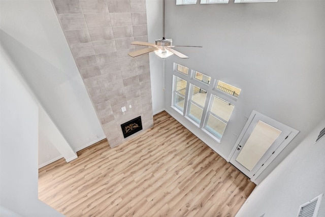 living room with a tile fireplace, ceiling fan, light hardwood / wood-style flooring, and a towering ceiling