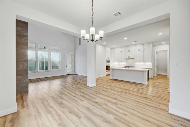 interior space featuring sink, hanging light fixtures, light hardwood / wood-style floors, a center island with sink, and a notable chandelier