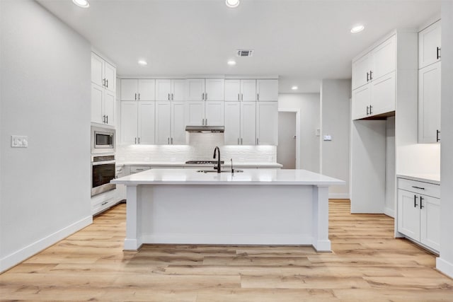 kitchen with white cabinetry, an island with sink, light hardwood / wood-style floors, and appliances with stainless steel finishes